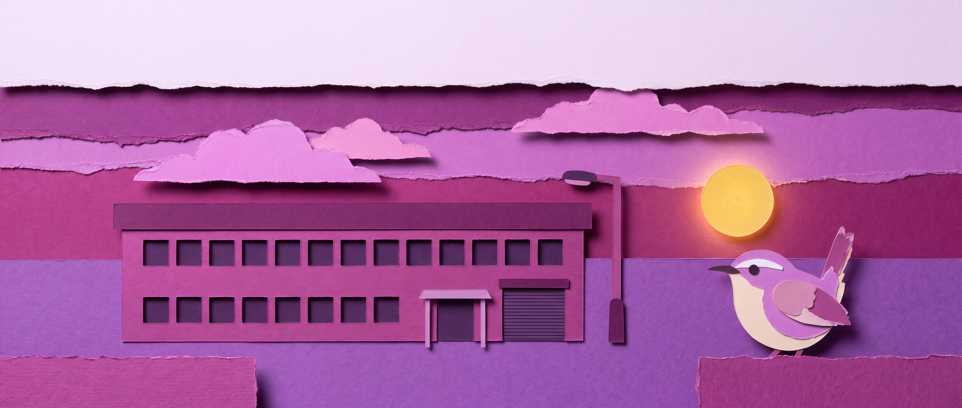 Cut-paper scene: a dark low-rise commercial building with an unlit lamppost and a small bird on the wall